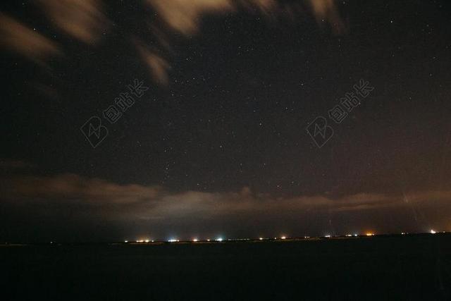 黑色夜空下流动的云和远处城市灯光背景图片