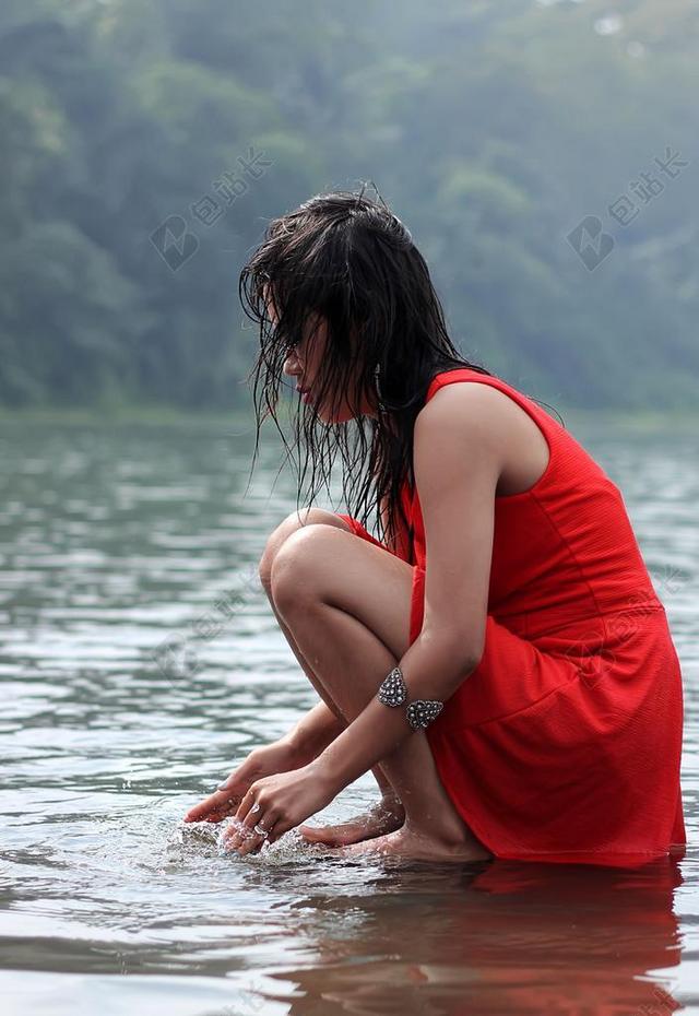 红色裙子少女蹲在小河里背景图片
