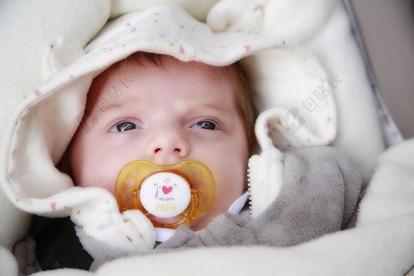 新生儿睁着大眼睛吸着奶嘴躺在床上背景图片