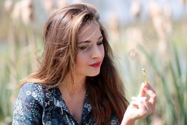 美丽的时尚的年轻的田园中的金发美女看花朵背景图片