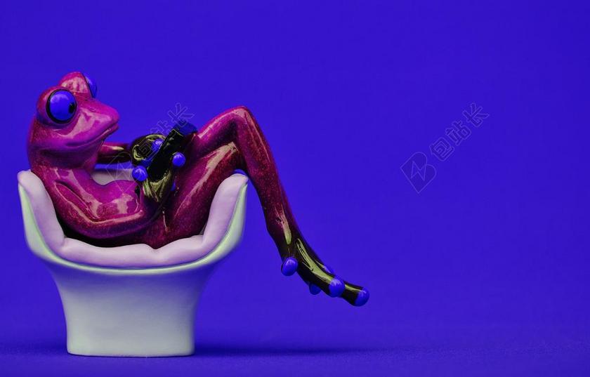 玩具沙发上玩手机的青蛙玩偶背景图片