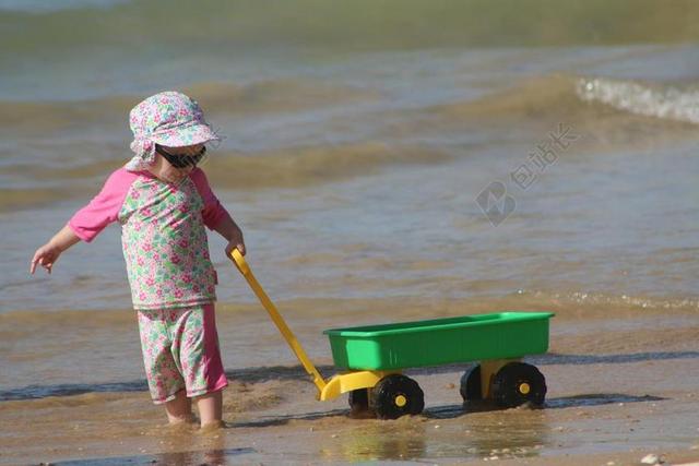 广告活泼可爱小孩子在海边玩推车宣传背景图片