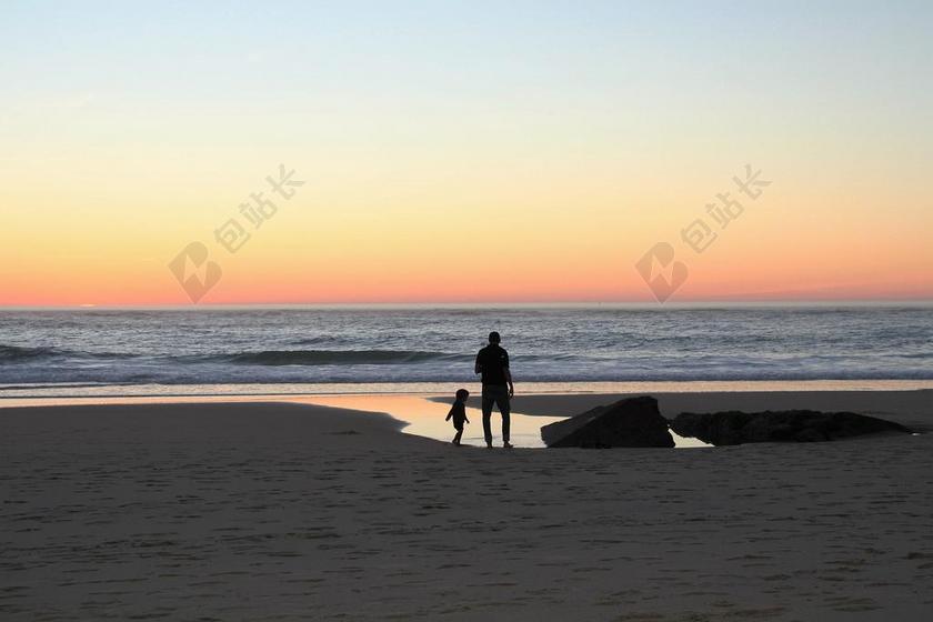 日落父亲带着孩子在在沙滩上背影图片
