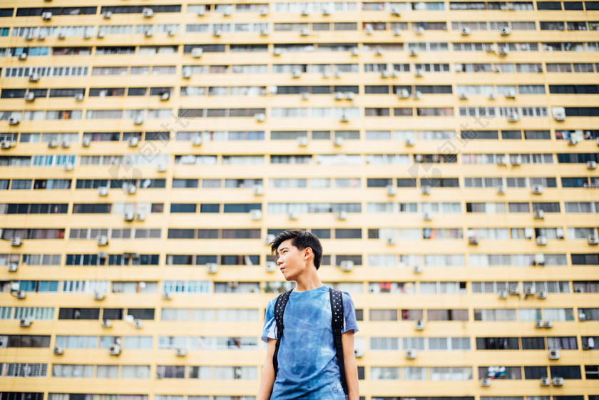 。黄蓝人物渺小巨大住宅区下的蓝衣男子人物街拍背景图片