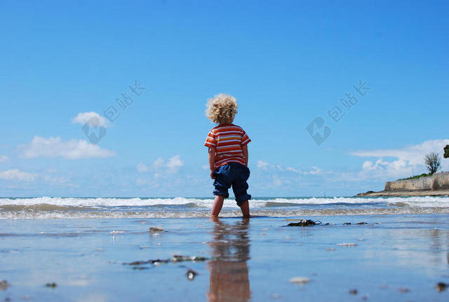 人物可爱蓝天下海滩上的卷发男孩儿童大海旅游背景图片